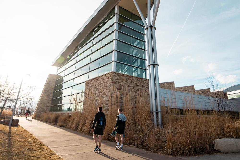 A photo of two students walking outside of the Student Recreation Center in the fall