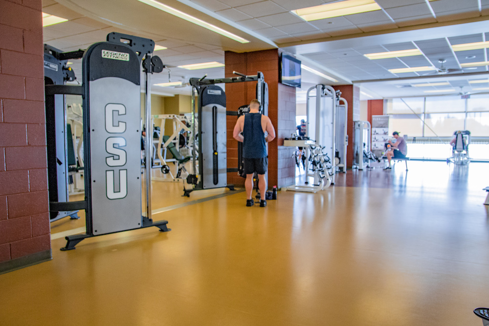 A photo of the upstairs facility and patrons lifting weights.